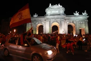 Aficionados celebran con una bandera de Espana frente a la Puerta de Alcala