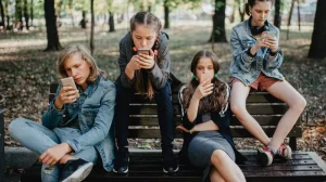 Adolescentes sentados en una banca mientras usan telefonos moviles