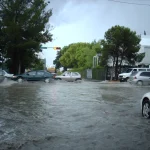 Vehículos avanzan por una calle anegada tras lluvia intensa
