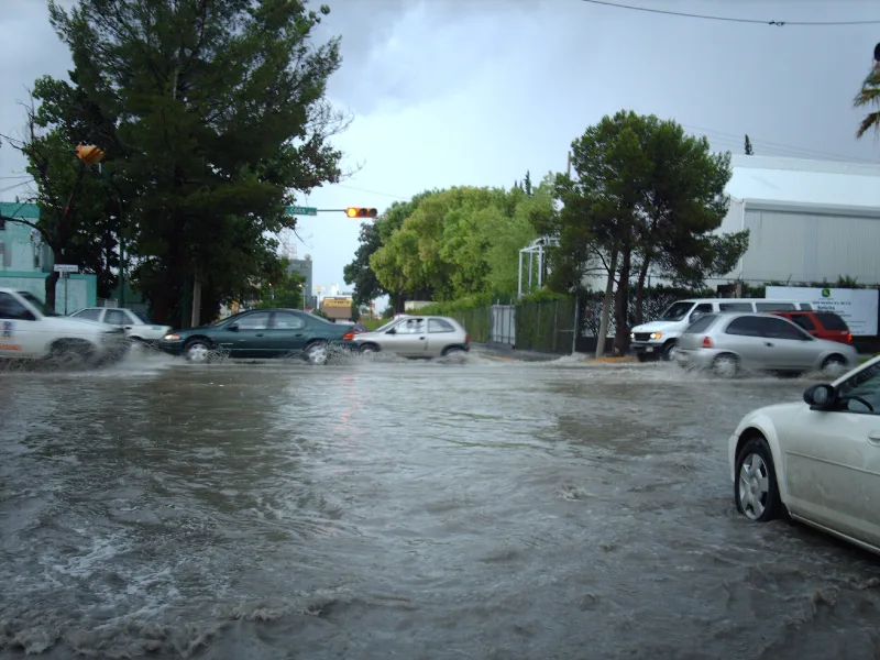 Vehículos avanzan por una calle anegada tras lluvia intensa