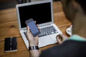 Persona usando telefono inteligente junto a una computadora portatil